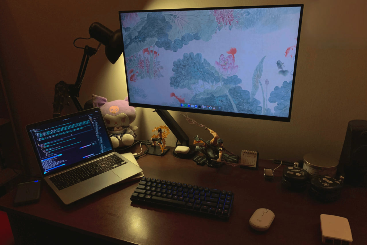 Rajin's desk with a monitor, two laptops, keyboard, speakers, figures, headphones, and accessories